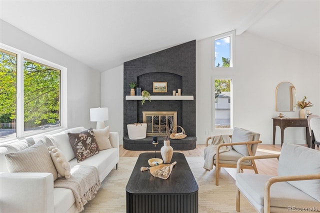 living room with a brick fireplace, a wealth of natural light, light hardwood / wood-style floors, and lofted ceiling with beams