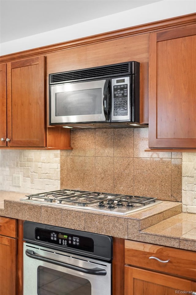 628 Cherry St, Denver, CO 80220 - kitchen featuring appliances with stainless steel finishes, tile counters, backsplash, and brown cabinets
