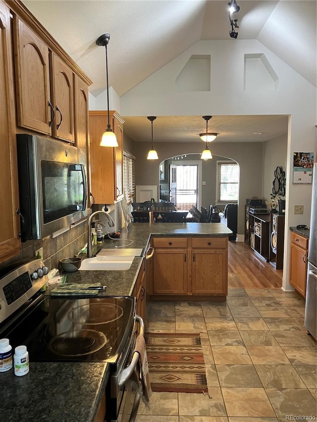 kitchen featuring appliances with stainless steel finishes, kitchen peninsula, pendant lighting, sink, and vaulted ceiling