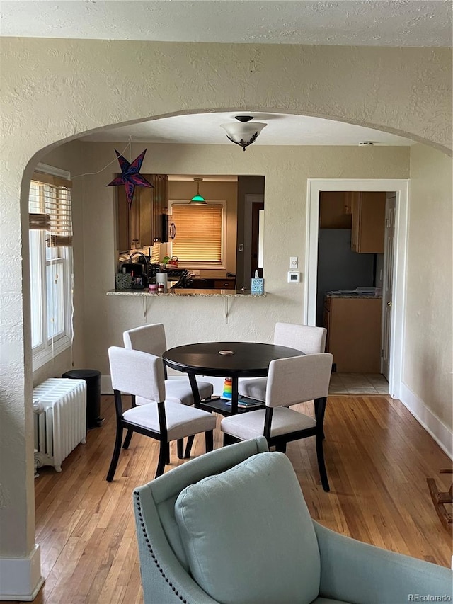 dining area with a textured ceiling, light hardwood / wood-style floors, and radiator