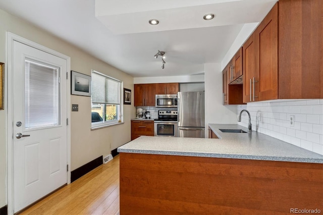 kitchen featuring decorative backsplash, kitchen peninsula, sink, light wood-type flooring, and appliances with stainless steel finishes