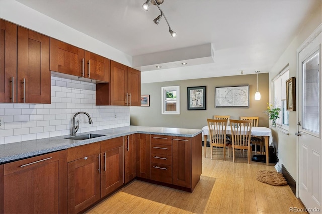 kitchen with decorative backsplash, hanging light fixtures, kitchen peninsula, sink, and light wood-type flooring