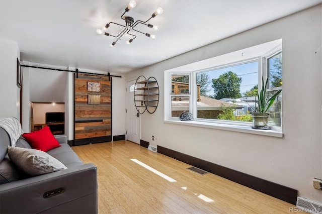 living room featuring a notable chandelier, light hardwood / wood-style flooring, and a barn door