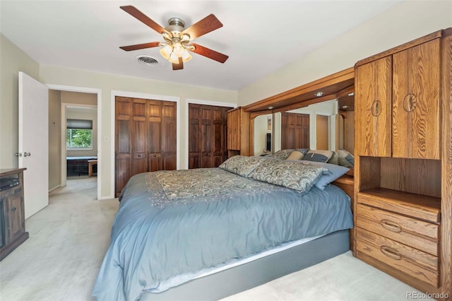 bedroom featuring visible vents, light carpet, two closets, and ceiling fan