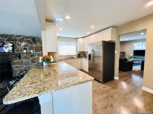 kitchen featuring stainless steel refrigerator with ice dispenser, a kitchen bar, light stone counters, kitchen peninsula, and white cabinets