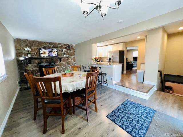 dining space featuring a notable chandelier, a stone fireplace, and light wood-type flooring