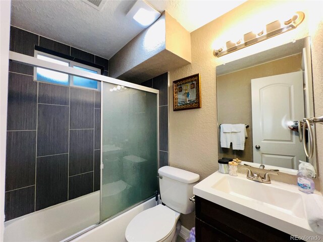 full bathroom featuring enclosed tub / shower combo, vanity, toilet, and a textured ceiling