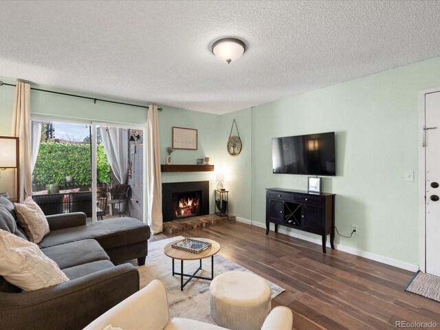 living room featuring wood finished floors, a textured ceiling, baseboards, and a warm lit fireplace