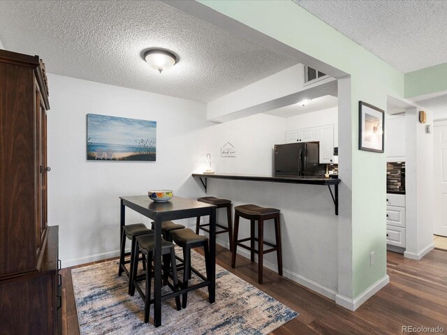 dining space featuring a textured ceiling, dark wood-style flooring, and baseboards