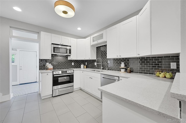 kitchen featuring backsplash, white cabinets, appliances with stainless steel finishes, light stone countertops, and light tile patterned floors