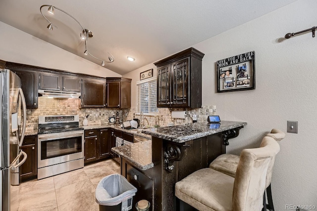 kitchen with kitchen peninsula, dark stone countertops, vaulted ceiling, a breakfast bar area, and appliances with stainless steel finishes