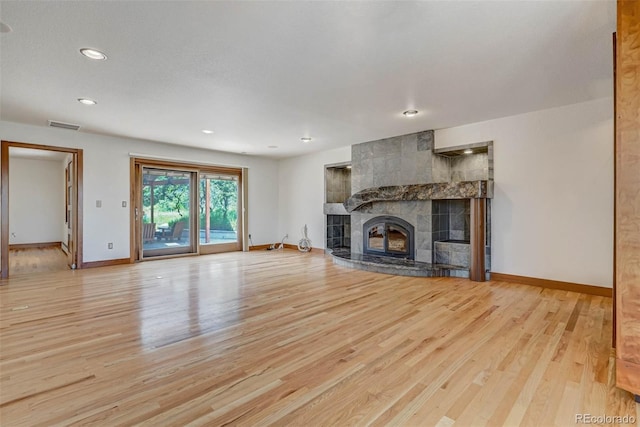 unfurnished living room with light wood-type flooring and a tiled fireplace