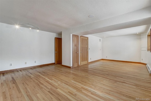 empty room featuring a baseboard heating unit, a textured ceiling, and light hardwood / wood-style flooring