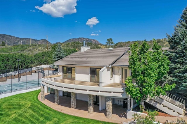 rear view of property with a lawn, a mountain view, a patio area, and a balcony