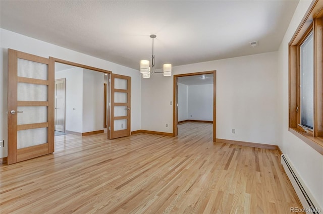 empty room featuring french doors, an inviting chandelier, light hardwood / wood-style floors, and a baseboard heating unit