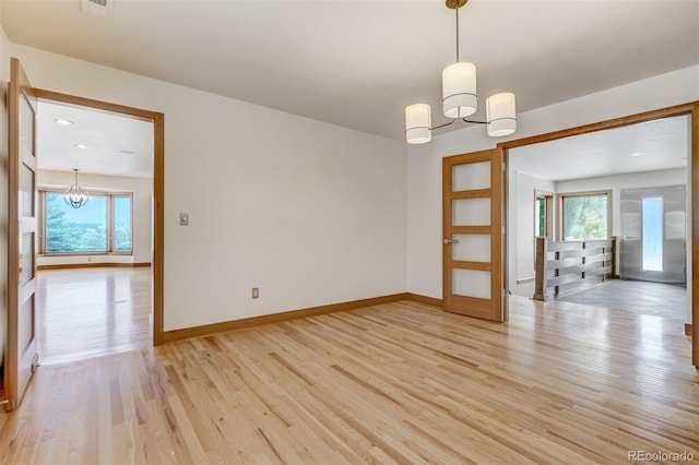 empty room with light hardwood / wood-style flooring and an inviting chandelier