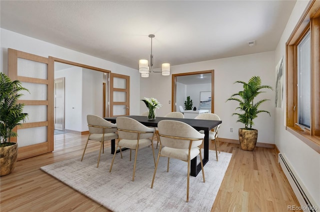 dining room featuring light wood-type flooring, a baseboard radiator, and an inviting chandelier