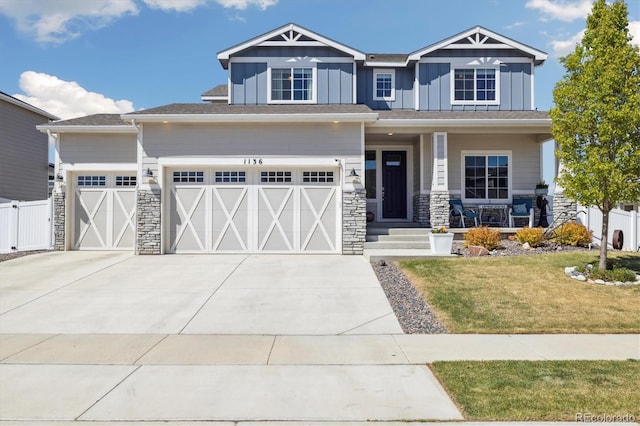 craftsman-style house featuring board and batten siding, driveway, covered porch, stone siding, and a front yard