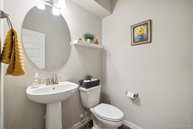 half bathroom featuring a sink, toilet, baseboards, and wood finished floors