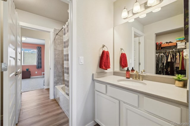 bathroom with shower / tub combo, baseboards, vanity, wood finished floors, and a spacious closet