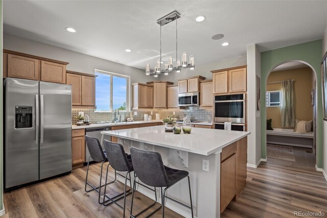 9389 Mayflower Gulch Way, Colorado Springs, CO 80927 - kitchen with stainless steel appliances, decorative backsplash, a kitchen island, wood finished floors, and light countertops