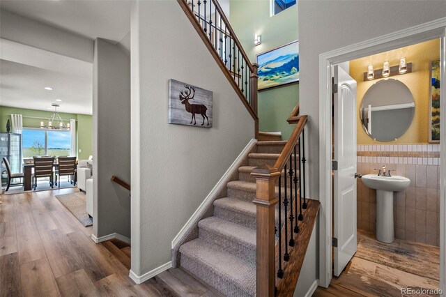 9389 Mayflower Gulch Way, Colorado Springs, CO 80927 - staircase featuring wood finished floors, a chandelier, wainscoting, tile walls, and baseboards