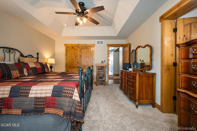 carpeted bedroom featuring ceiling fan and a raised ceiling