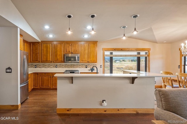 kitchen with appliances with stainless steel finishes, tasteful backsplash, hanging light fixtures, and an island with sink