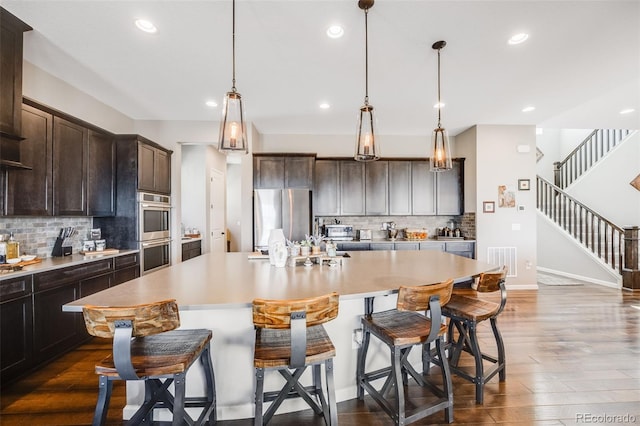 kitchen with dark wood-style flooring, visible vents, appliances with stainless steel finishes, a kitchen island, and dark brown cabinets