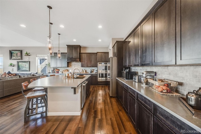 kitchen featuring dark wood-type flooring, open floor plan, a sink, dark brown cabinetry, and a kitchen breakfast bar