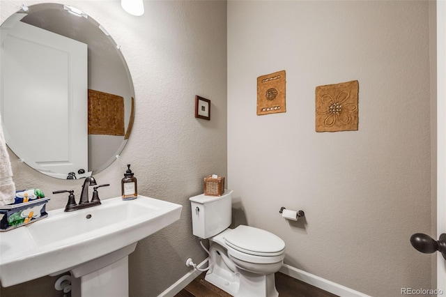 half bath featuring a textured wall, toilet, a sink, wood finished floors, and baseboards