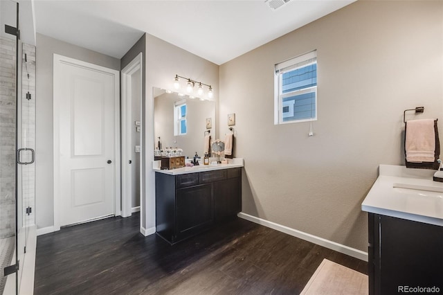 full bathroom featuring a stall shower, baseboards, two vanities, and wood finished floors