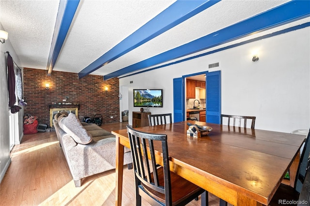 9700 E Iliff Ave Unit E51, Denver, CO 80231 - dining area featuring a textured ceiling, beam ceiling, light wood-style floors, a fireplace, and brick wall