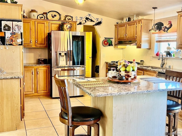 kitchen featuring pendant lighting, sink, light tile patterned floors, stainless steel fridge, and a breakfast bar area