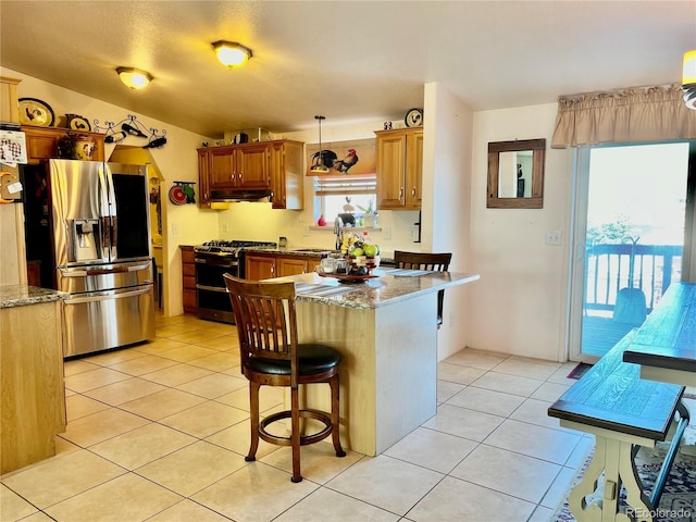 kitchen featuring light tile patterned flooring, decorative light fixtures, a kitchen breakfast bar, stainless steel appliances, and light stone countertops