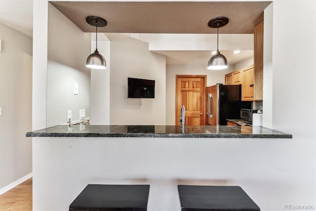 kitchen with wood finished floors, baseboards, a peninsula, freestanding refrigerator, and pendant lighting