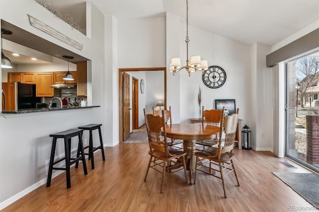 dining area with visible vents, baseboards, light wood-style flooring, an inviting chandelier, and a towering ceiling