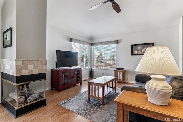 living area with wood finished floors, baseboards, a multi sided fireplace, and ceiling fan