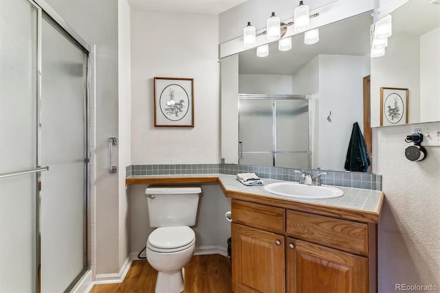 bathroom featuring a shower stall, toilet, decorative backsplash, wood finished floors, and vanity