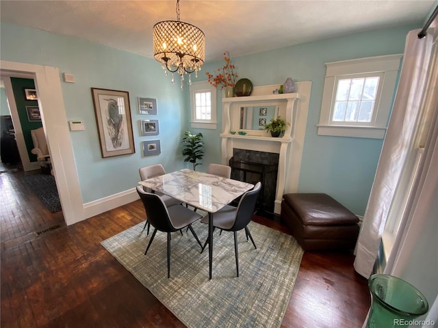 dining space featuring a fireplace with flush hearth, baseboards, an inviting chandelier, and hardwood / wood-style flooring