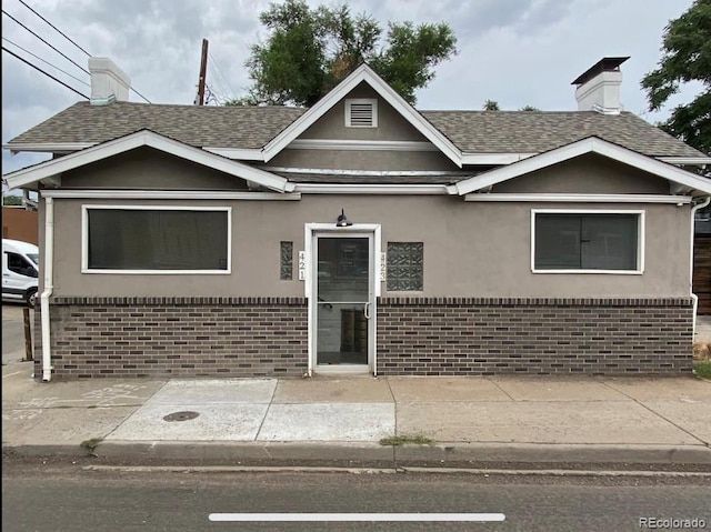 view of front of house with brick siding, stucco siding, and roof with shingles