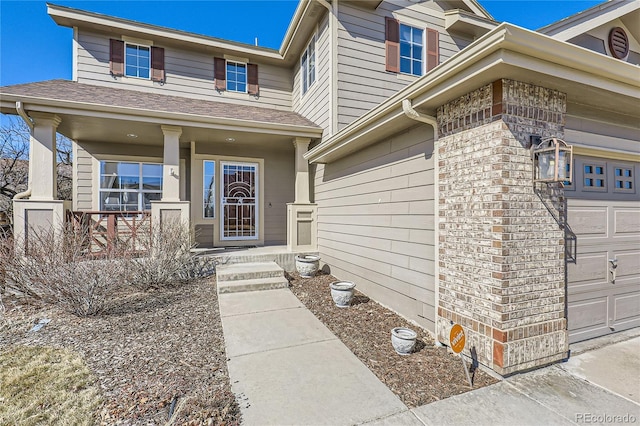 property entrance with an attached garage, covered porch, roof with shingles, and brick siding