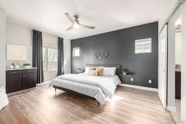 bedroom featuring baseboards, a ceiling fan, an accent wall, and light wood finished floors
