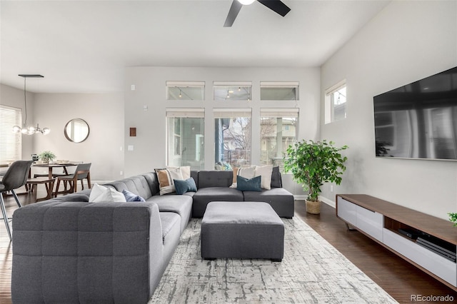 living room with dark wood-type flooring, ceiling fan with notable chandelier, and baseboards