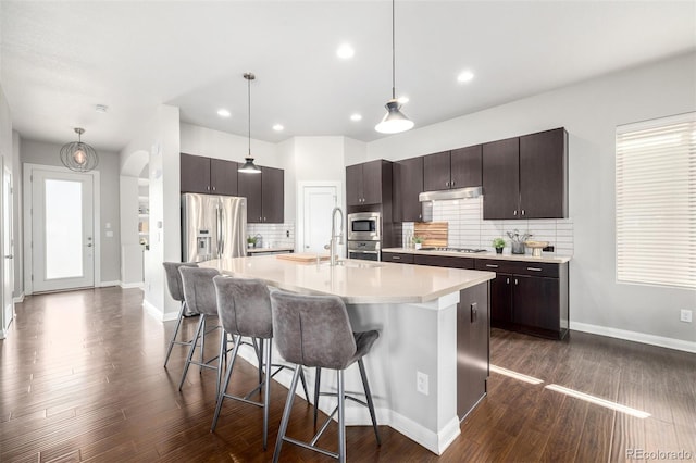 kitchen with dark brown cabinetry, a kitchen bar, light countertops, dark wood-style floors, and stainless steel appliances