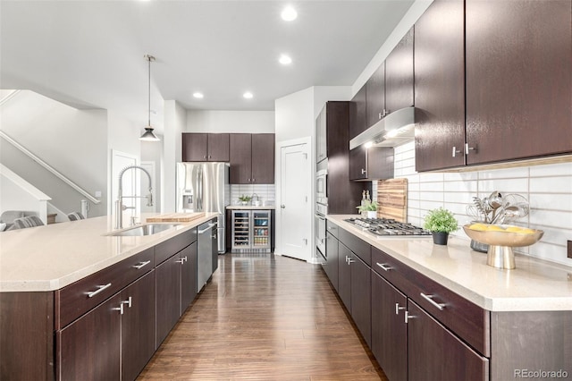 kitchen with dark wood-style flooring, a sink, stainless steel appliances, dark brown cabinets, and under cabinet range hood