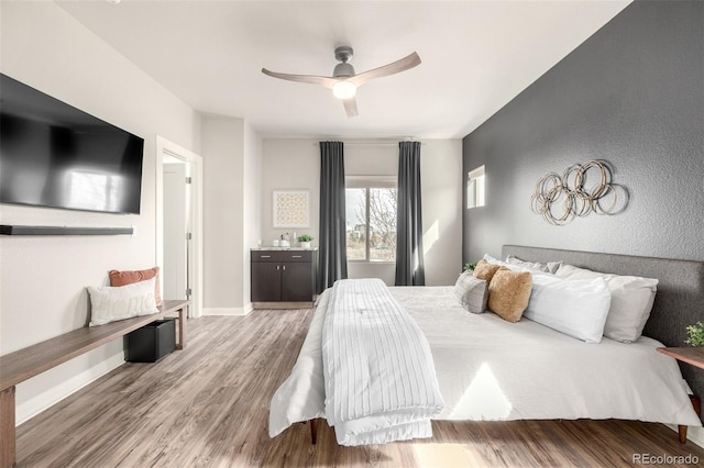 bedroom featuring a textured wall, a ceiling fan, baseboards, and wood finished floors