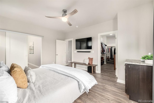 bedroom with a spacious closet, baseboards, light wood-style floors, a closet, and a ceiling fan