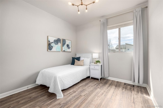 bedroom featuring visible vents, a notable chandelier, wood finished floors, and baseboards