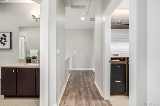 corridor with visible vents, an upstairs landing, a sink, light wood-style floors, and baseboards